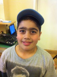 Atila står i ett klassrum. Han har en keps och en grå t-shirt.