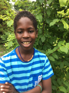 Andrew ler i sin blårandiga tröja framför en grön buske.