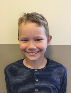 Nikolas ler stort. Han har kort ljust hår och en smårandig grå tröja.