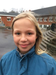 Bim ler mot kameran. Hon har blå jacka och långt blont hår som blåser i vinden.