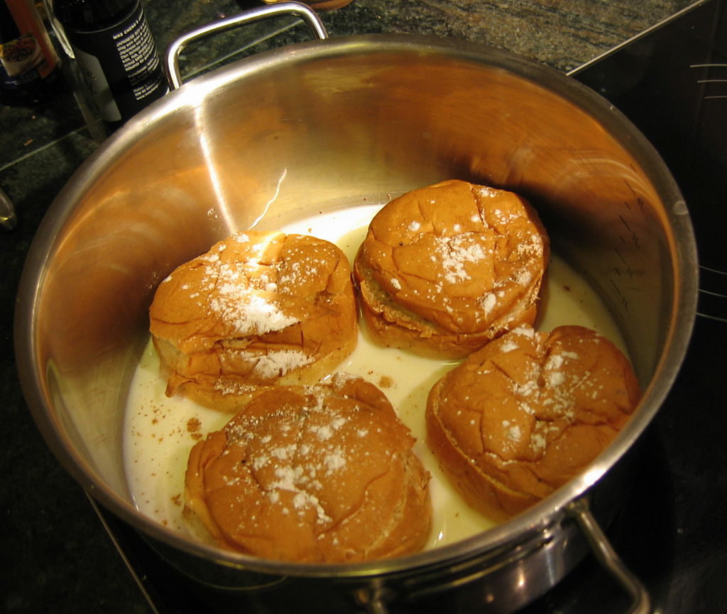 Fyra semmelbullar som ligger i en gryta med mjölk.