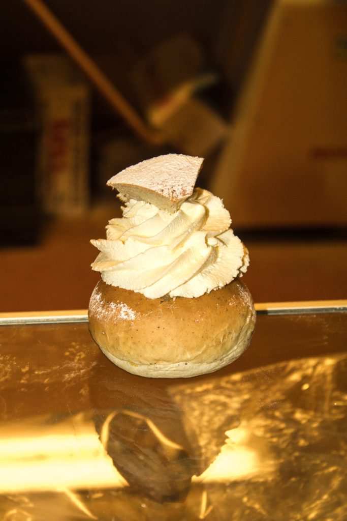 En vanlig semla står på ett bord. Den har mycket grädda och ett trekantigt lock.