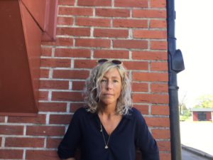 En person med svart skjorta står mot en röd tegelvägg.