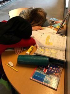 Två barn som ligger och sover på skrivbordet bland flera läxböcker.