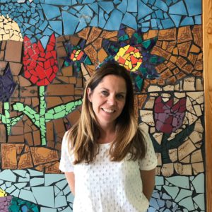 En lärare ler mot kameran. Bakgrunden är färgglad med ett motiv av blommor.