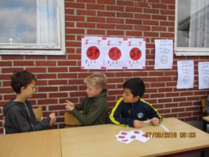 Tre barn vid ett bord intill skolans tegelvägg.