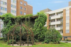 En spaljé intill buskage och höghus.