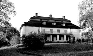 Svartvit bild på ett stort hus med trädgård framför.