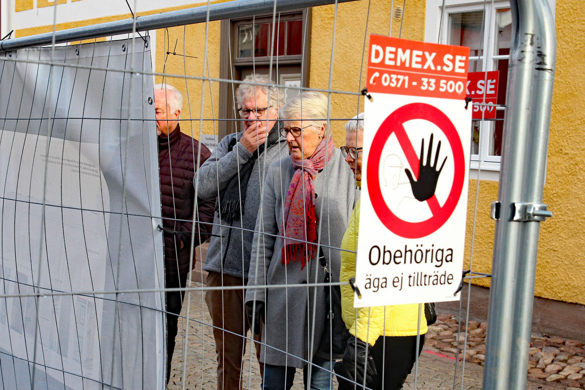 Flera gamla personer står utanför ett staket och tittar förfärat in genom staketet. På staketet sitter det en skylt där det står "Obehöriga äga ej tillträde".