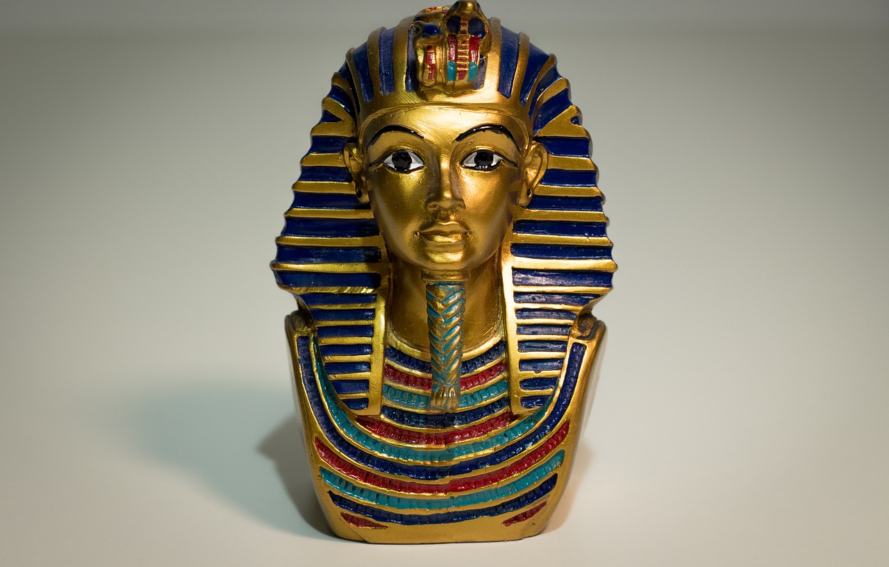 En guldig staty av Tutankhamun. Han har skägg på hakan som är flätat och över hans hår ligger som en duk som också är randig av guld.