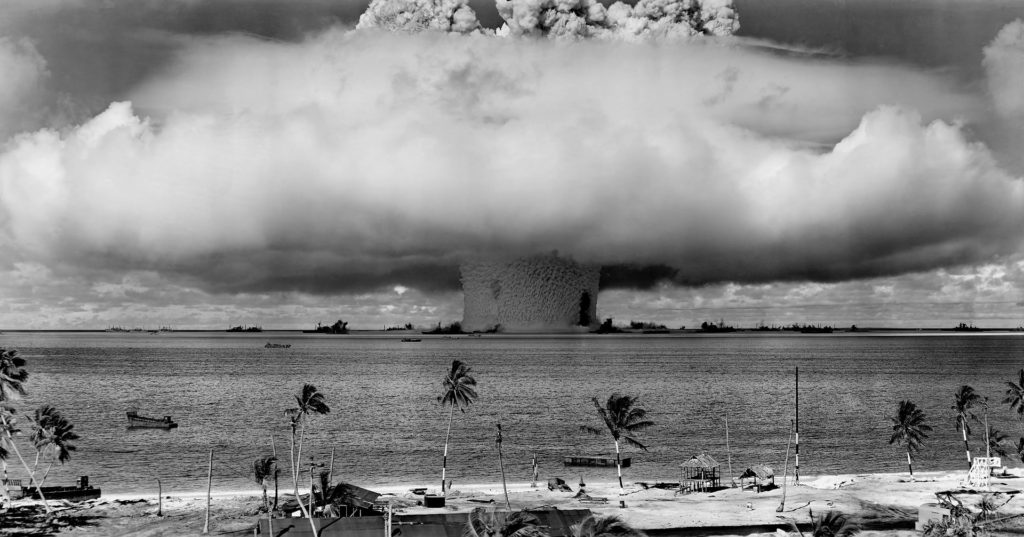En atombomb sprängs i fjärran. Ett stort svampliknande moln stiger mot himlen.