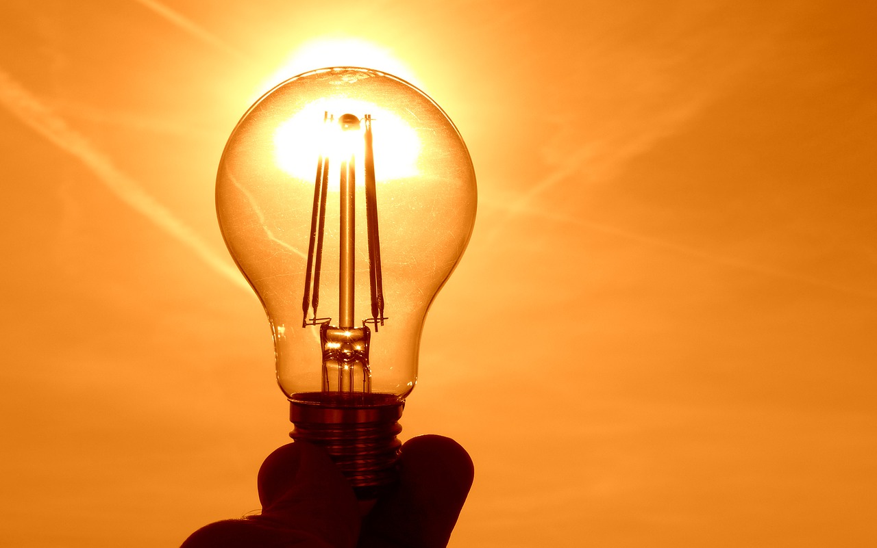 En hand håller i en glödlampa som soler lyser genom.