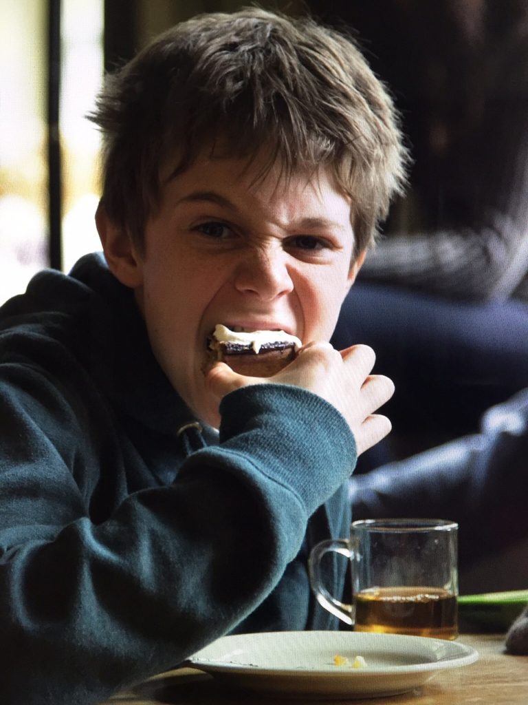 Ett barn som äter en kaka. Han tittar in i kameran samtidigt som han tar ett bett och ser lite galen ut.