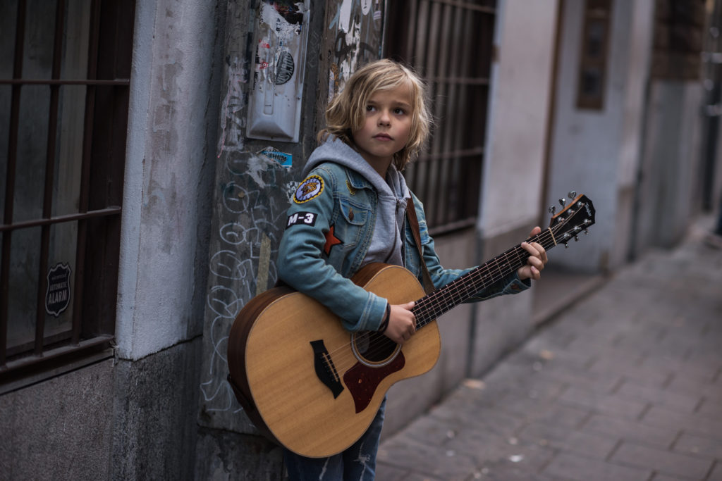 Oscar står på en gata med en gitarr i famnen