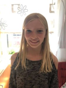 Ella har långt rakt hår och tittar in i kameran med ett stort leende.