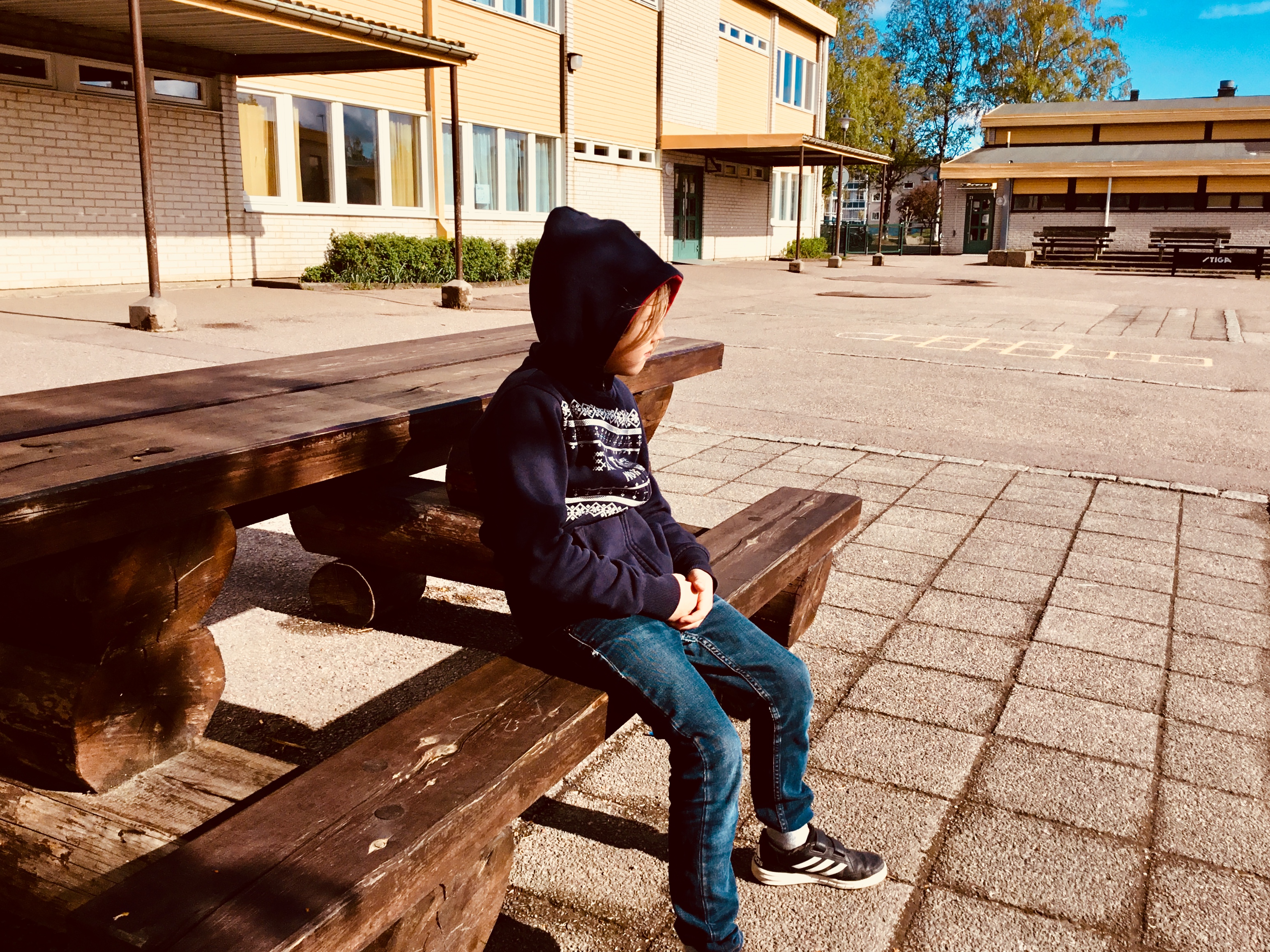 Ett barn sitter på en bänk i solen på en skolgård.