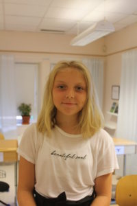 Selma står i ett klassrum. Hon har långt hår ner till axlarna och ler litegrann.