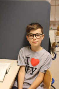 Vincent sitter mot en vägg i ett klassrum. Han ser ut att vara påväg att säga något. Han har kort hår och glasögon med kraftiga bågar.