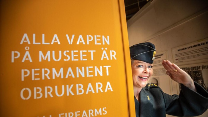En utklädd skådespelare på museet står bredvid en skylt på vilken det står "Alla vapen på museet är permanent obrukbara"