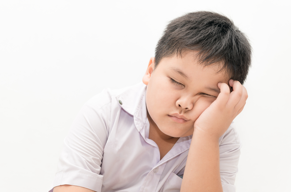 Ett barn sitter med huvudet i handen och sover.