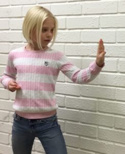 Tjej framför en vit tegelmur visar ett karateslag.