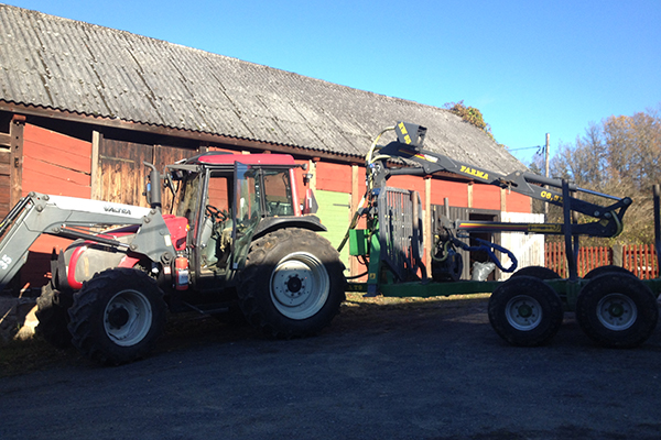 En Valtra står uppställd framför en röd ladugård.