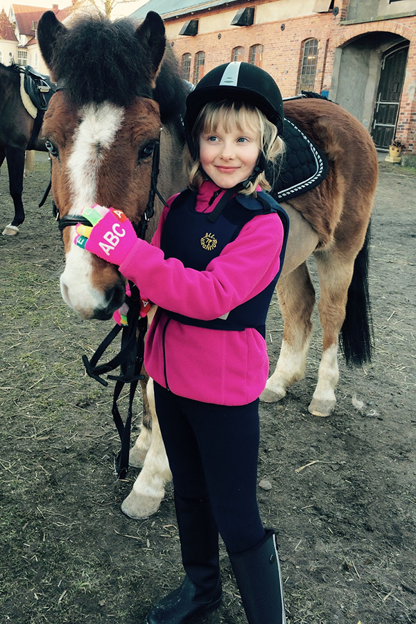 En ridtjej i rosa tröja klappar en brun häst på mulen.