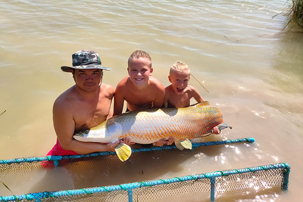 Oskar står i vattnet tillsammans med guiden och sin lillebror. Tillsammans håller de i en jättestor fisk.