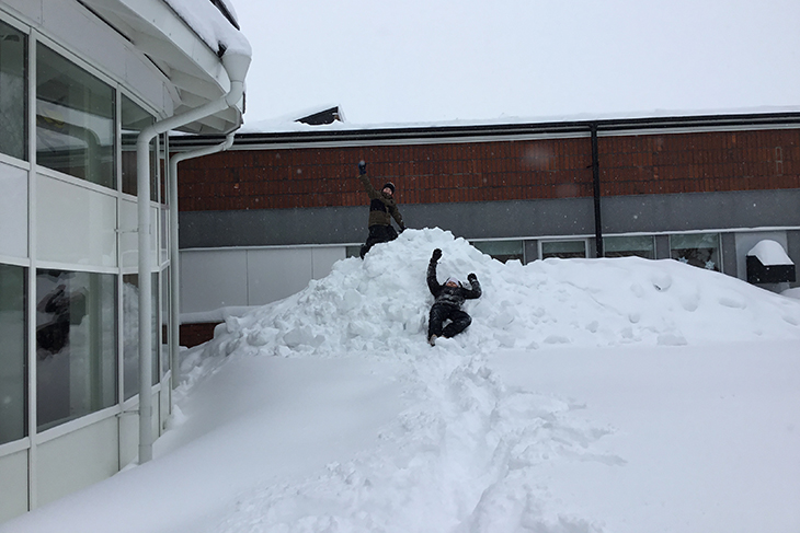 Två elever som leker i en stor snöhög.