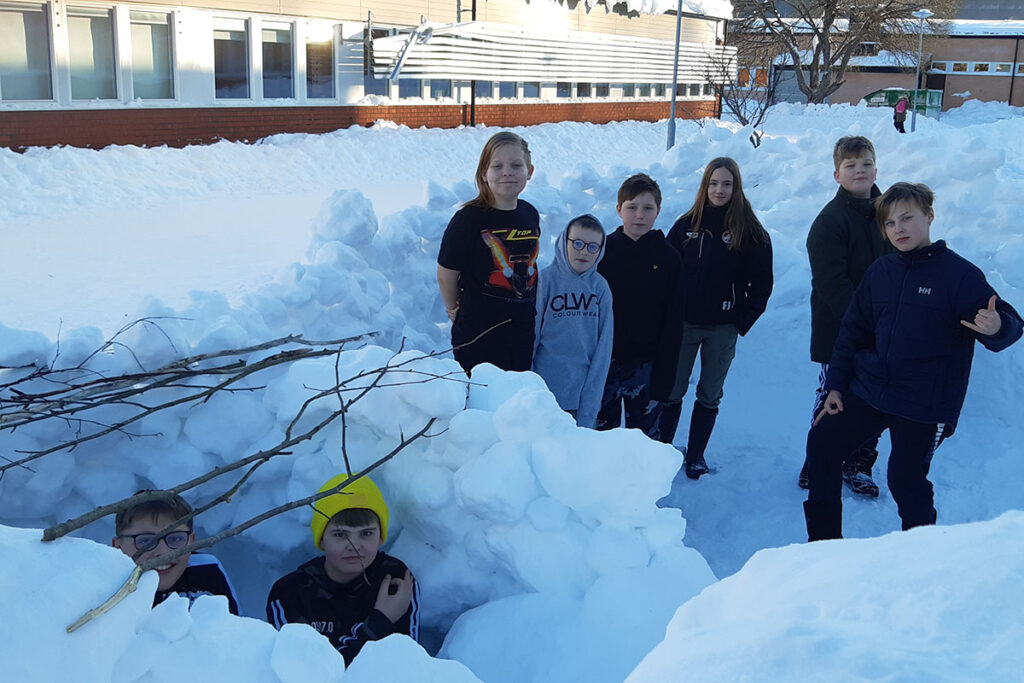 Elever från Pitholmsskolan som står i snön vid sin snöborg.