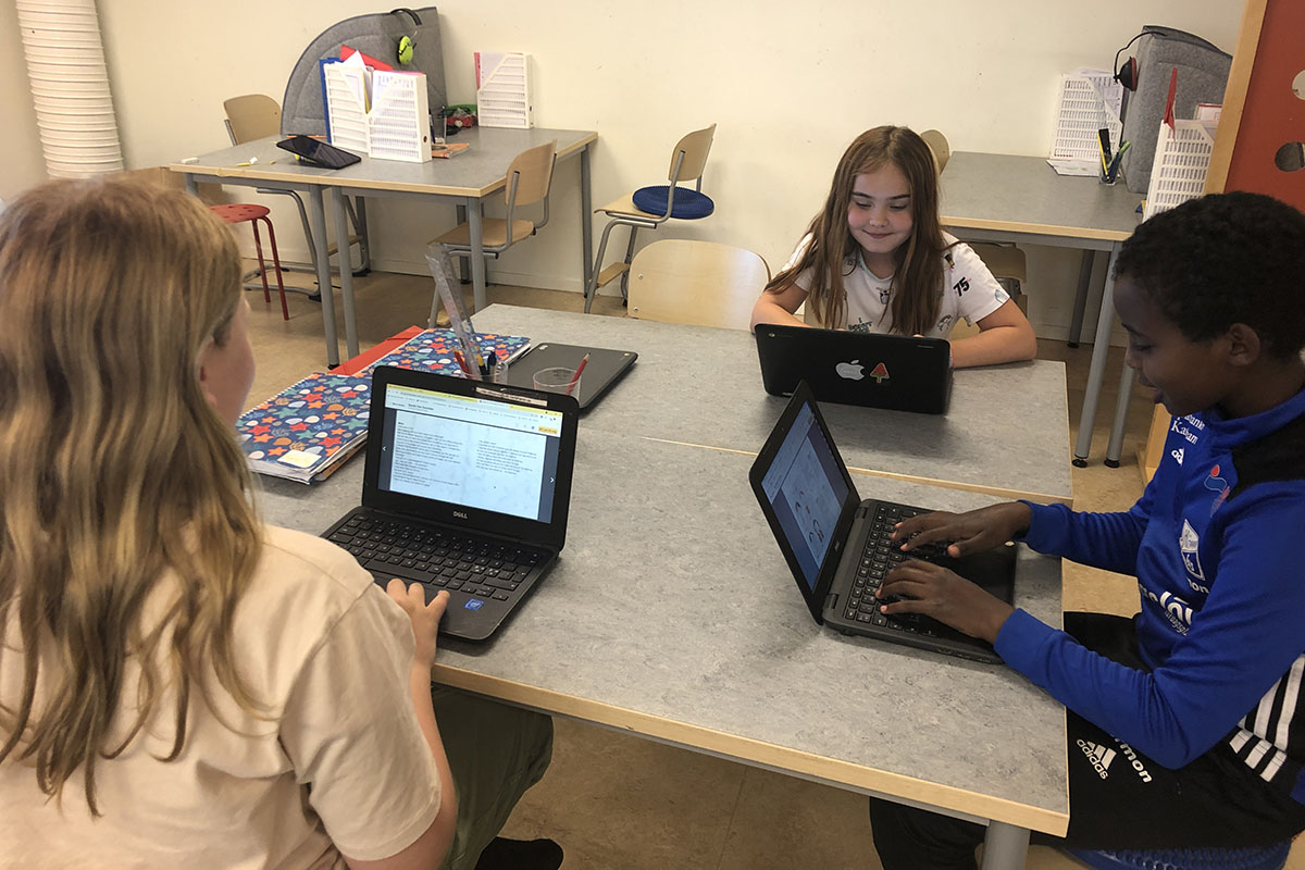 Tre elever som sitter vid ett bord med sina datorer.