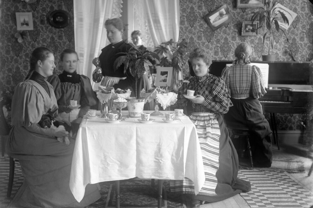 Damer som fikar. De sitter vid ett bord med vit duk på.